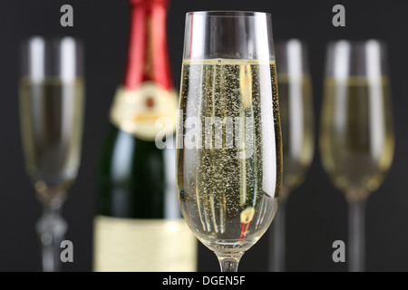 Champagner mit Luftblasen in einem Glas mit einer Flasche und mehr Gläser im Hintergrund Stockfoto