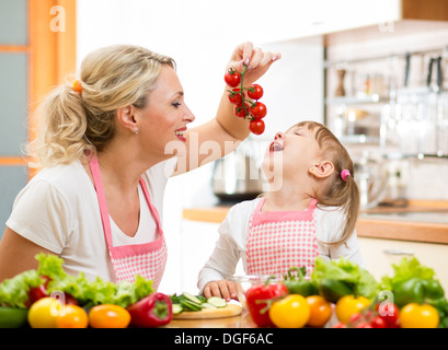 Mutter Vorbereitung Abendessen und Fütterung Kind Tomate in Küche Stockfoto