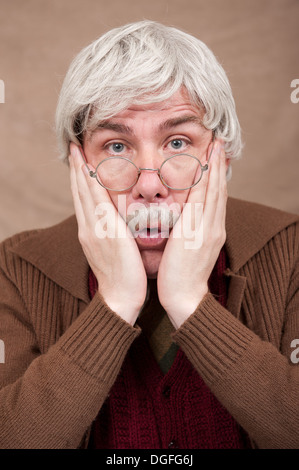 Schockierter, grauhaariger alter Mann, mit beiden Händen auf dem Gesicht, der gerade auf die Kamera blickt. Stockfoto