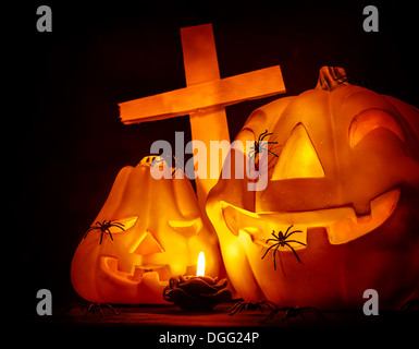 Closeup auf glühenden geschnitzten Kürbis mit gruselige Spinnen auf dem Friedhof, geheimnisvolle Kreuz auf dunklen Halloween-Nacht Stockfoto