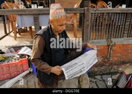 Mann mit traditionellen Kopfbedeckungen Zeitunglesen, Taumadhi Square, Bhaktapur, Kathmandu-Tal, Nepal, Asien Stockfoto