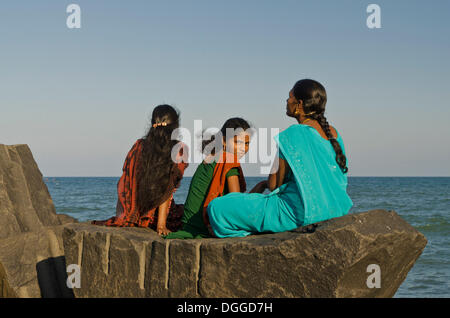 Drei junge Damen sitzen auf einem Felsen am Strand von Pondicherry, Blick auf das Meer, Pondicherry, Indien, Asien Stockfoto