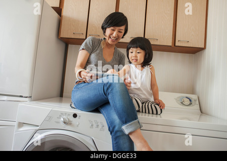 Mutter und Tochter sitzen auf Waschmaschine mit tablet Stockfoto