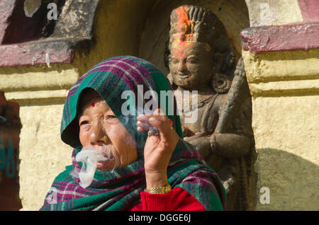 Alte Frau, Rauchen, vor einer Statue, Kathmandu, Kathmandu District, Bagmati Zone, Nepal Stockfoto
