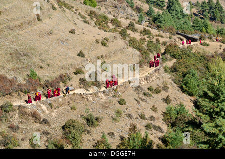 Mönche und Nonnen tragen rote Tücher zu Fuß auf einem schmalen Pfad entlang einem Berg Hang, Junbesi, Solukhumbu Bezirk Stockfoto