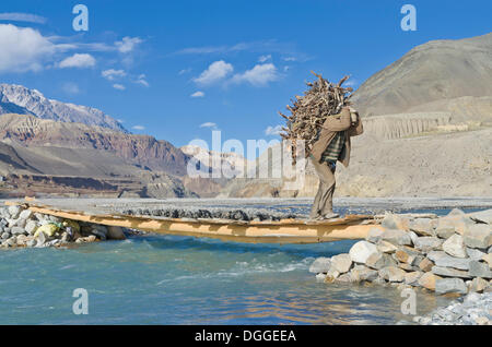 Mann mit Brennholz auf einer Brücke über den Kali Ghandaki Fluss, Kaghbeni, Mustang District, Nepal Stockfoto