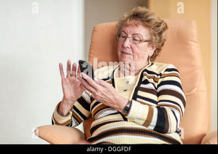 Ältere Frau in einem Sessel sitzend und mit einem smartphone Stockfoto