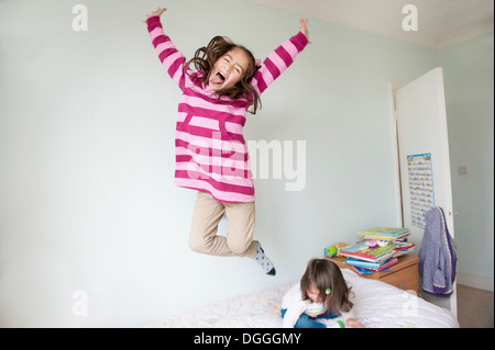 Mädchen springen auf Bett und Gesicht ziehen Stockfoto