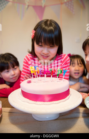 Mädchen betrachten Geburtstagskerzen auf Kuchen Stockfoto