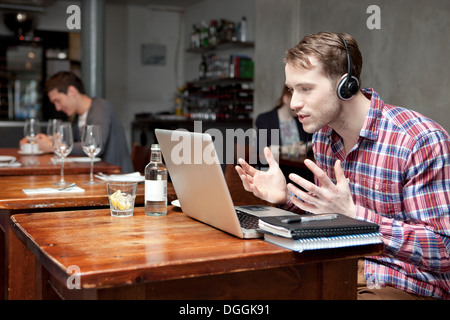 Junger Mann mit Kopfhörern mit Laptop im café Stockfoto