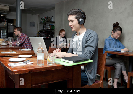 Junger Mann mit Kopfhörern mit Laptop im café Stockfoto