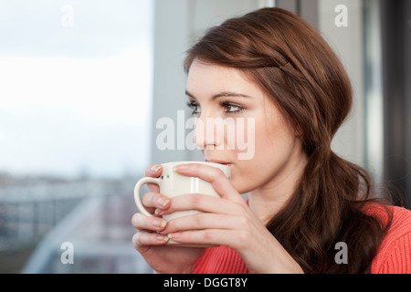 Junge Frau mit Kaffeetasse Blick aus Fenster Stockfoto