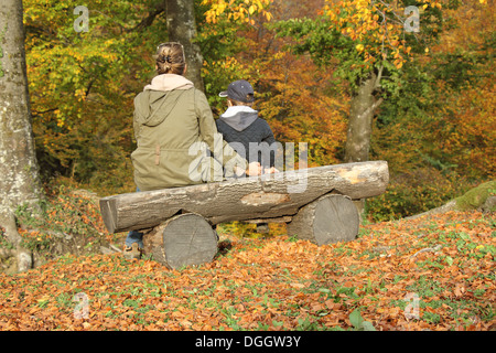 Mutter und Kind sitzt auf einer Bank im Wald an einem sonnigen Herbsttag Stockfoto