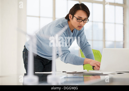 Mann mit Laptop mit Modellen von Windenergieanlagen auf Schreibtisch Stockfoto