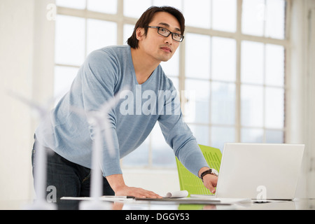 Mann mit Laptop mit Modellen von Windenergieanlagen auf Schreibtisch Stockfoto