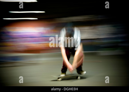 Ein Skateboarder fährt seinem Skateboard in der Nacht unter Kunstlicht auf London Southbank mit bunten Graffiti im Hintergrund. Stockfoto