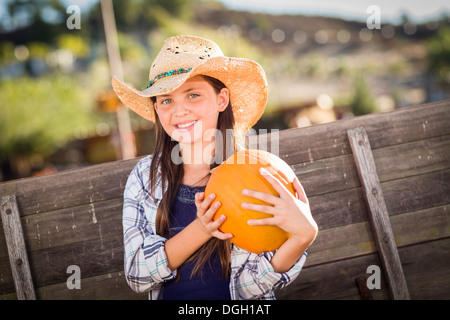 Preteen Mädchen tragen Cowboyhut Porträt im Kürbisbeet in rustikaler Umgebung. Stockfoto