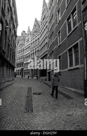 Ein Mann hält einen Regenschirm geht auf einer gepflasterten Straße (Kaasstraat) mit überragenden Eigenschaften in Antwerpen, Belgien. Stockfoto