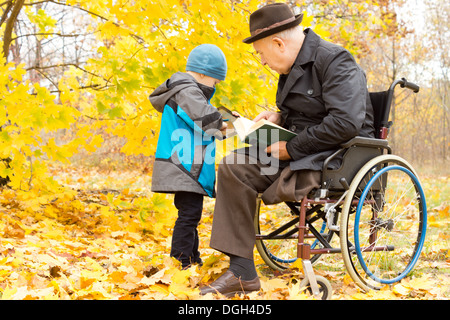 Kleines Kind mit seiner Behinderung Großvater, der hat ein Bein amputiert und sitzt im Rollstuhl, Austausch von Informationen über seine Stockfoto