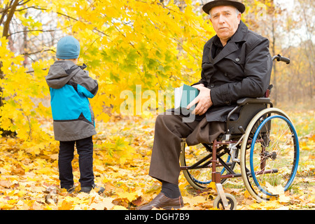 Behinderten älteren Mann mit einem Bein amputiert begleitet ein kleines Kind auf einen Tagesausflug in eine bunte gelb Herbst Park sitzen Stockfoto