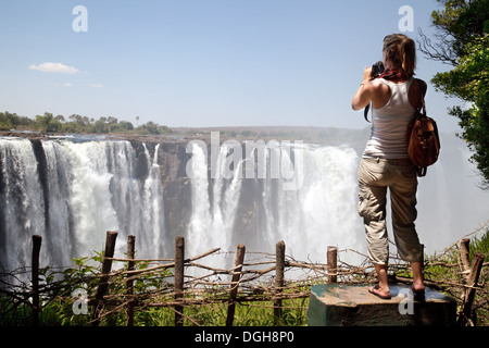 Alleinreise; Junge Touristin, die ein Foto der Victoria Falls, Hauptkatarakt, vom Victoria Falls National Park, Simbabwe, Afrika, machen möchte Stockfoto