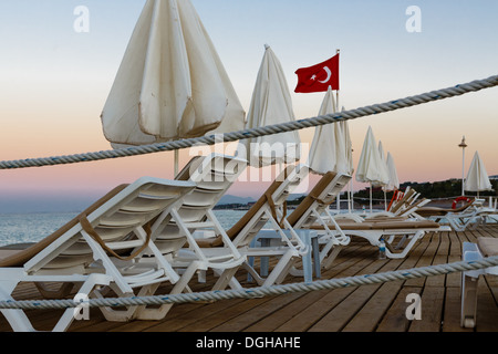 Liegestühle und Sonnenschutz Sonnenschirme auf einem hölzernen Pier in türkischen Resort auf einem Strand des Mittelmeers Stockfoto