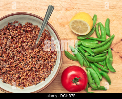 Zutaten für eine Vegatrian Mahlzeit, Inlcuding Quinoa, Gerste, Zwiebeln, Zitrone, Erbsen und Tomaten auf einer Holzoberfläche Stockfoto