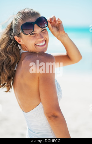 Porträt der lächelnde junge Frau im Badeanzug mit Sonnenbrille am Strand Stockfoto