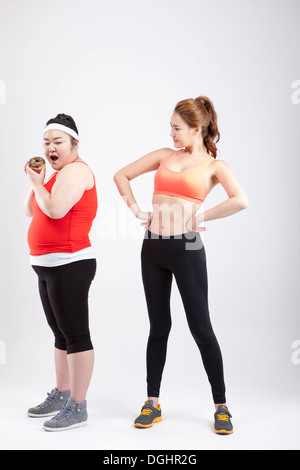 ein dickes Mädchen mit einem Donut und ein dünnes Mädchen in Sportkleidung Stockfoto