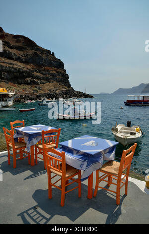 Tische und Stühle im Restaurant "Katína" im Ammoúdi Hafen von Oia, Santorini, Cyclades, griechische Inseln, Griechenland Stockfoto