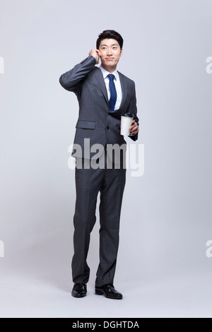 ein Business-Mann hält eine Kaffeetasse während des Gesprächs am Telefon Stockfoto