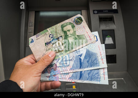 Nordirland 10 und 20-Pfund-Noten gehalten in einer Hand vor einem Geldautomaten, Nordirland, Vereinigtes Königreich Stockfoto