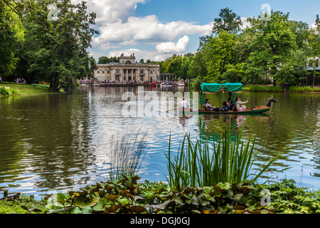 Touristen genießen eine Gondelfahrt auf dem See im Lazienki-Park in Warschau mit dem Palast im Hintergrund. Stockfoto