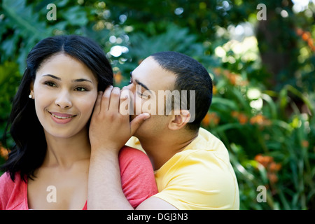 Junger Mann, die Frau ins Ohr flüstern Stockfoto