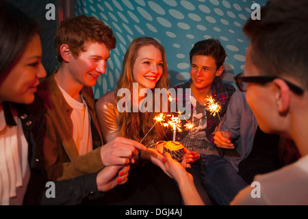 Gruppe von Jugendlichen, die herumsitzen und Geburtstagstorte mit Wunderkerzen Stockfoto