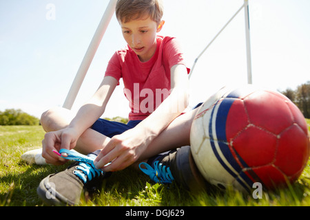 Junge sitzt auf Feld Schnürsenkel binden Stockfoto