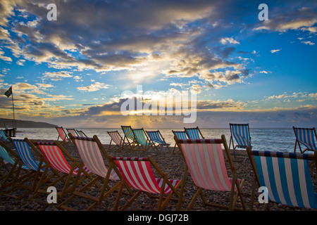 Leere Liegestühle bei Sonnenaufgang am Strand von Bier in Devon. Stockfoto