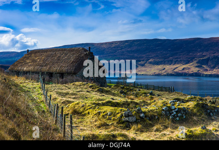 Eine traditionelle Blackhouse in der Nähe von Uig auf der Isle Of Skye mit Ruinen der alten Gebäude im Vordergrund. Stockfoto