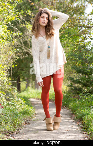 Junge Frau trägt einen langen weißen Pullover und rote Strumpfhose im freien Stockfoto