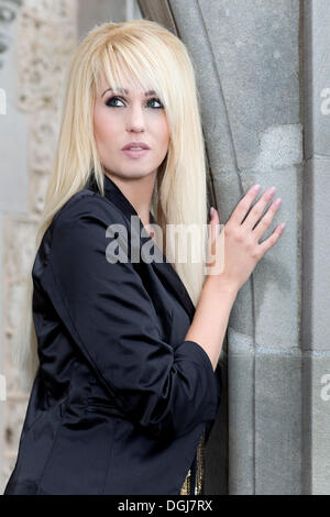 Junge Frau mit langen blonden Haaren trug eine schwarze Jacke posiert in einem steinernen Torbogen, Porträt Stockfoto