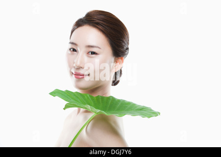 eine Frau posiert mit einem grünen Blatt über die Schulter Stockfoto
