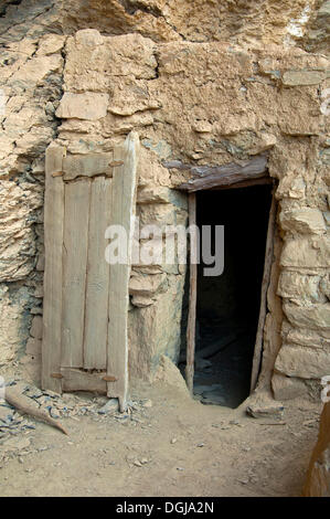 Eingang mit einer geschnitzten Holztür, eine Steinhütte in der verlassenen Siedlung von Sap Bani Khamis unter einem Felsvorsprung in der Stockfoto