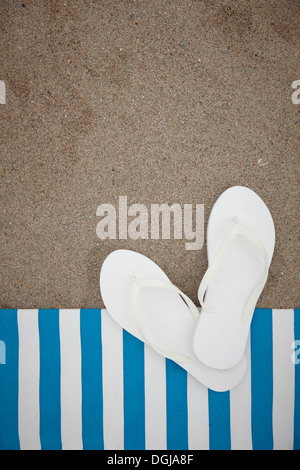 ein paar weiße Flip flops auf einem Handtuch am Strand Stockfoto