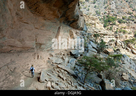 Lokale Wanderer unter einem Überhang Felsen auf dem Weg in die verlassene Siedlung von Sap Bani Khamis an der Westflanke des gehen die Stockfoto