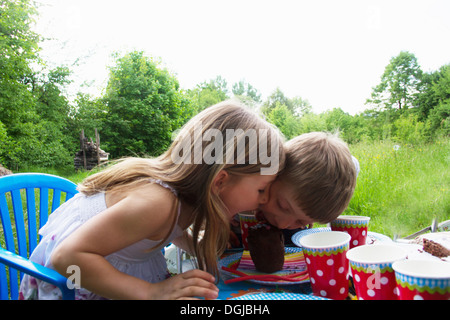 Bruder und Schwester im Wettbewerb um Kuchen an Picknick-Tisch Stockfoto