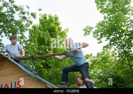 Vater und zwei Kinder klettern auf Spielhaus Dach Stockfoto