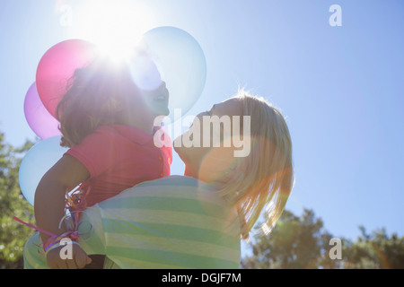 Mutter umarmt Tochter im Sonnenlicht mit Korb des Ballons Stockfoto