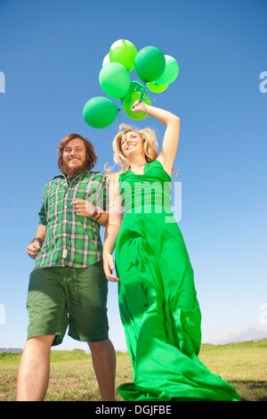 Junges Paar im Feld, Frau mit grünen Ballons Stockfoto
