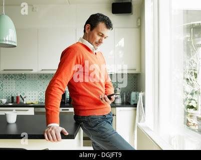 Reifer Mann mit Handy in Küche Stockfoto