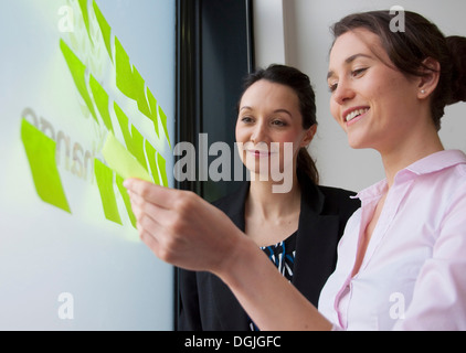 Weiblichen Kollegen kleben Klebefuge Notizen auf Glas Stockfoto